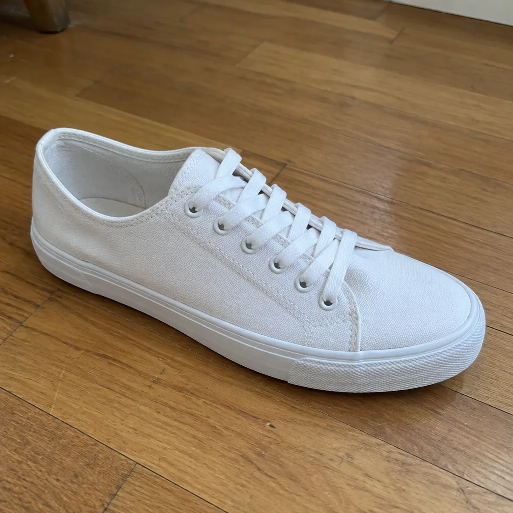 Plain white canvas sneaker on a wooden floor