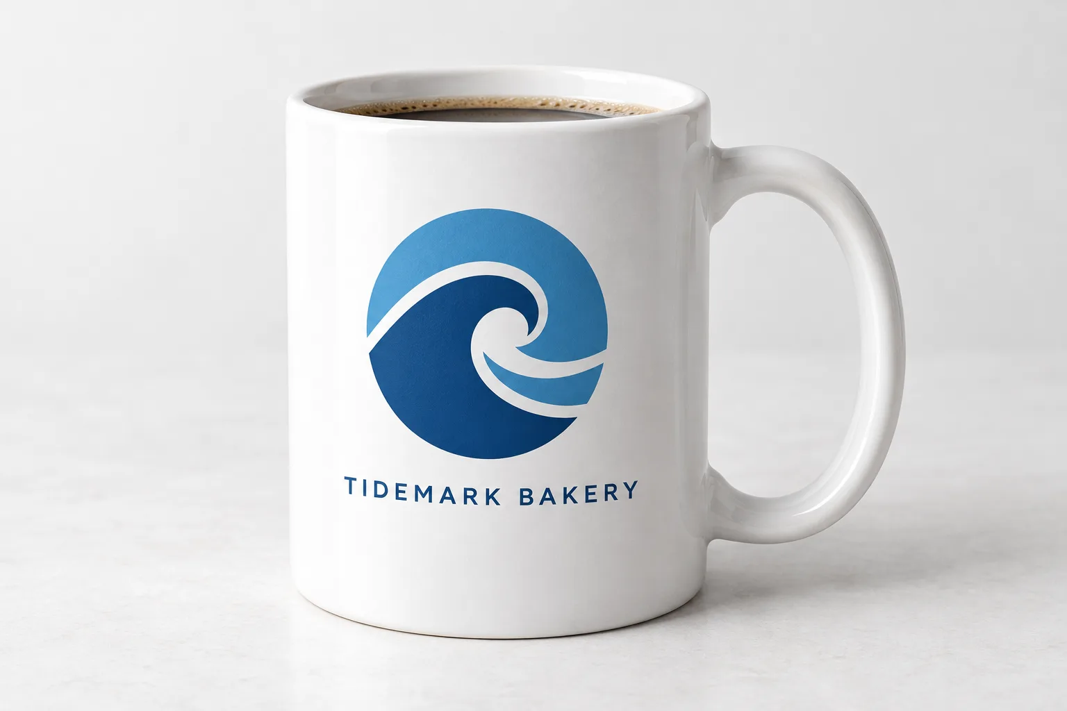 The TIDEMARK BAKERY logo printed on a white coffee mug filled with coffee