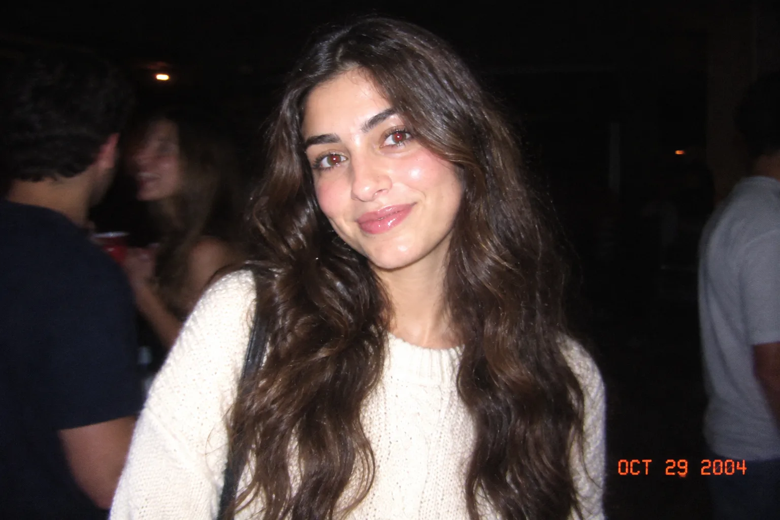 The same woman at a crowded night party in a flash snapshot with an orange date stamp in the corner